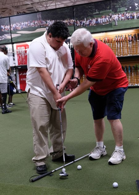 A volunteer helps a participant line up a golf swing at an indoor driving range