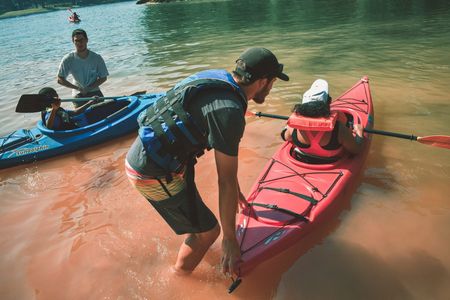 A volunteer helps launch a kayak while another participant paddles nearby