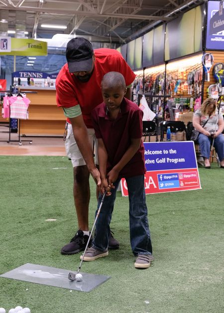 A volunteer coaches a young participant on his golf swing