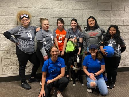 The Atlanta women's goalball team poses together, including a player with a guide dog