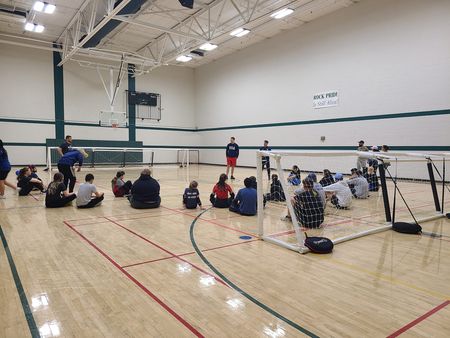 Athletes and volunteers gather in the gym for a goalball clinic