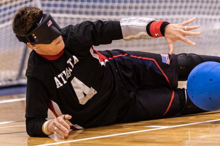 A goalball player in an Atlanta jersey dives to block the ball during a match