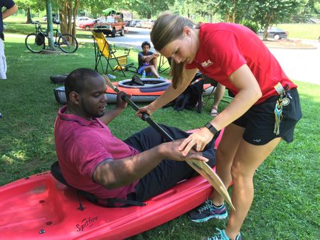 A volunteer helps a participant launch a kayak at the water's edge