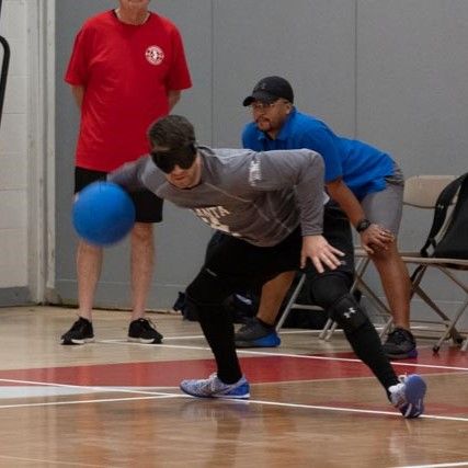 A goalball player dives to block a shot as teammates and officials look on