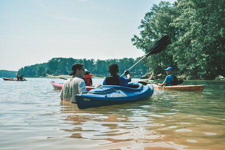 A group of kayakers paddle together on a lake surrounded by trees