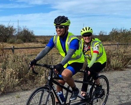 Two tandem cycling riders in safety vests ride together on a paved trail