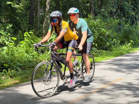 Two tandem cycling riders smile for the camera on a wooded trail