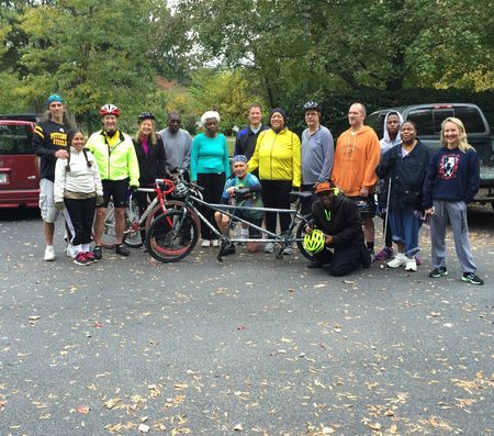 A group of tandem cycling riders pedal together down a tree-lined path in fall